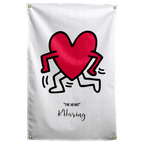 A red heart with black outlined arms and legs dances above small THE HEART lettering on pale cream on a Wall Rebel fabric wall flag.