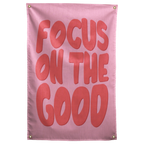 Large rounded coral Focus on the Good lettering fills a pink background on this upbeat Wall Rebel fabric wall flag.