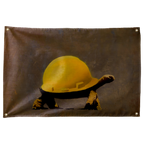 A tortoise wears an oversized yellow construction hard hat against brown-grey on this humorous horizontal Wall Rebel fabric wall flag.