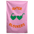 Green heart-shaped sunglasses and orange Hater Blockers lettering stand out on this pink Wall Rebel fabric wall flag.