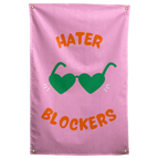 Green heart-shaped sunglasses and orange Hater Blockers lettering stand out on this pink Wall Rebel fabric wall flag.