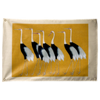 Black-and-white cranes stand across an ochre field, surrounded by a pale cream border on a Wall Rebel fabric wall flag.