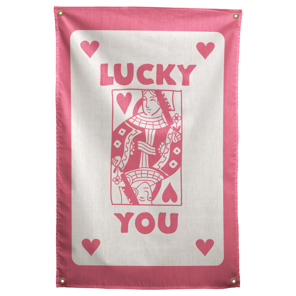 Pink LUCKY YOU lettering, corner hearts and a queen-card illustration sit on cream within a pink border on a Wall Rebel fabric wall flag.