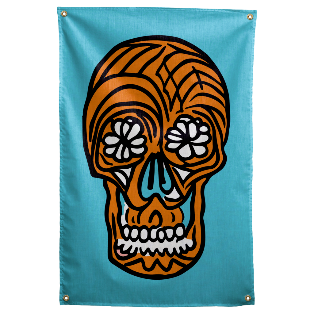 An orange skull with white floral eyes and thick black outlines floats on a turquoise background on a Wall Rebel fabric wall flag.