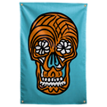 An orange skull with white floral eyes and thick black outlines floats on a turquoise background on a Wall Rebel fabric wall flag.