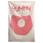 A pink-iced doughnut with sprinkles and a large bite sits below YUMMY lettering on this cream Wall Rebel fabric wall flag.